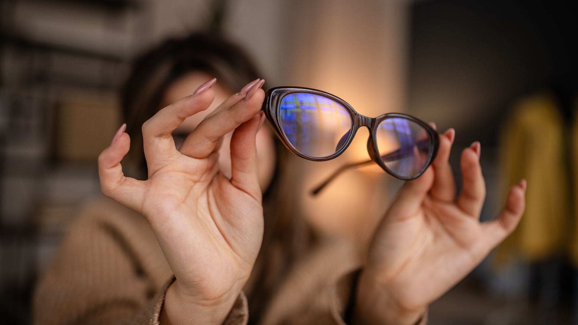 A woman holds up a pair of blue light blocking glasses.