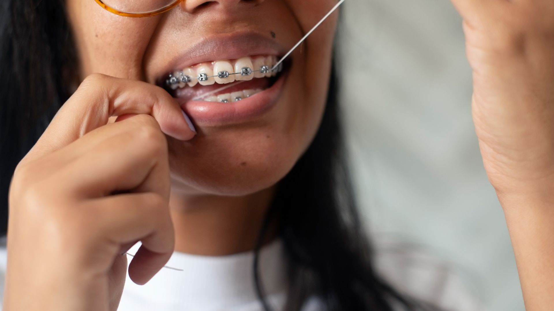 A young woman uses dental floss to clean between her braces and teeth.